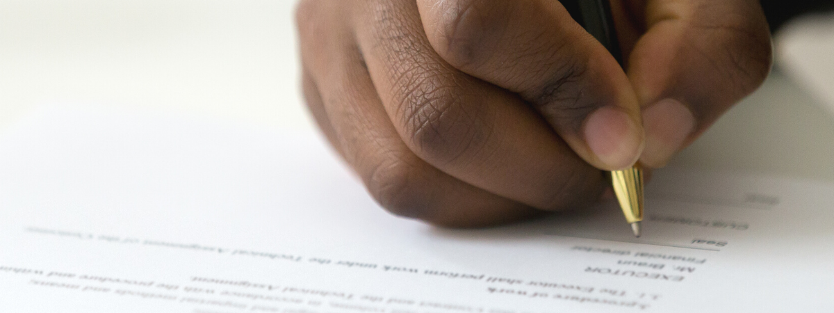 A man's hand holds a pen and signs a legal document