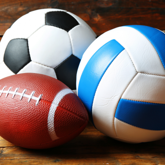 Soccer ball, football, and volleyball on a wooden surface.