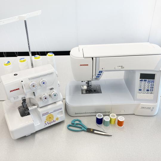 A serger and sewing machine with spools of thread and a pair of scissors. 