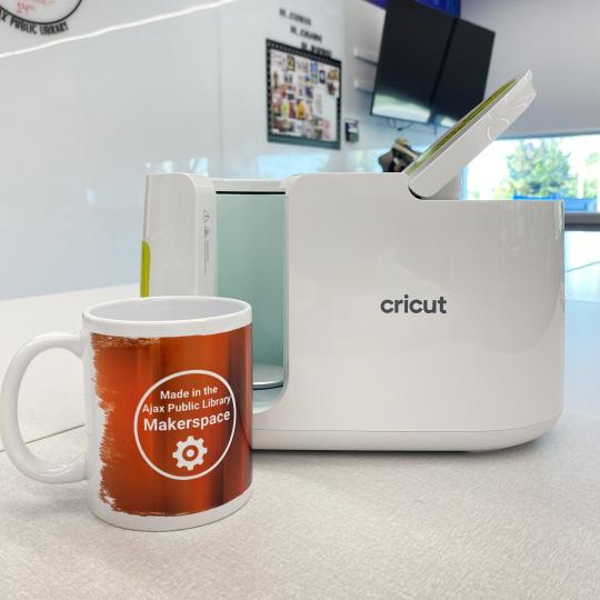 A ceramic mug with a custom design and mug heat press in the background. 